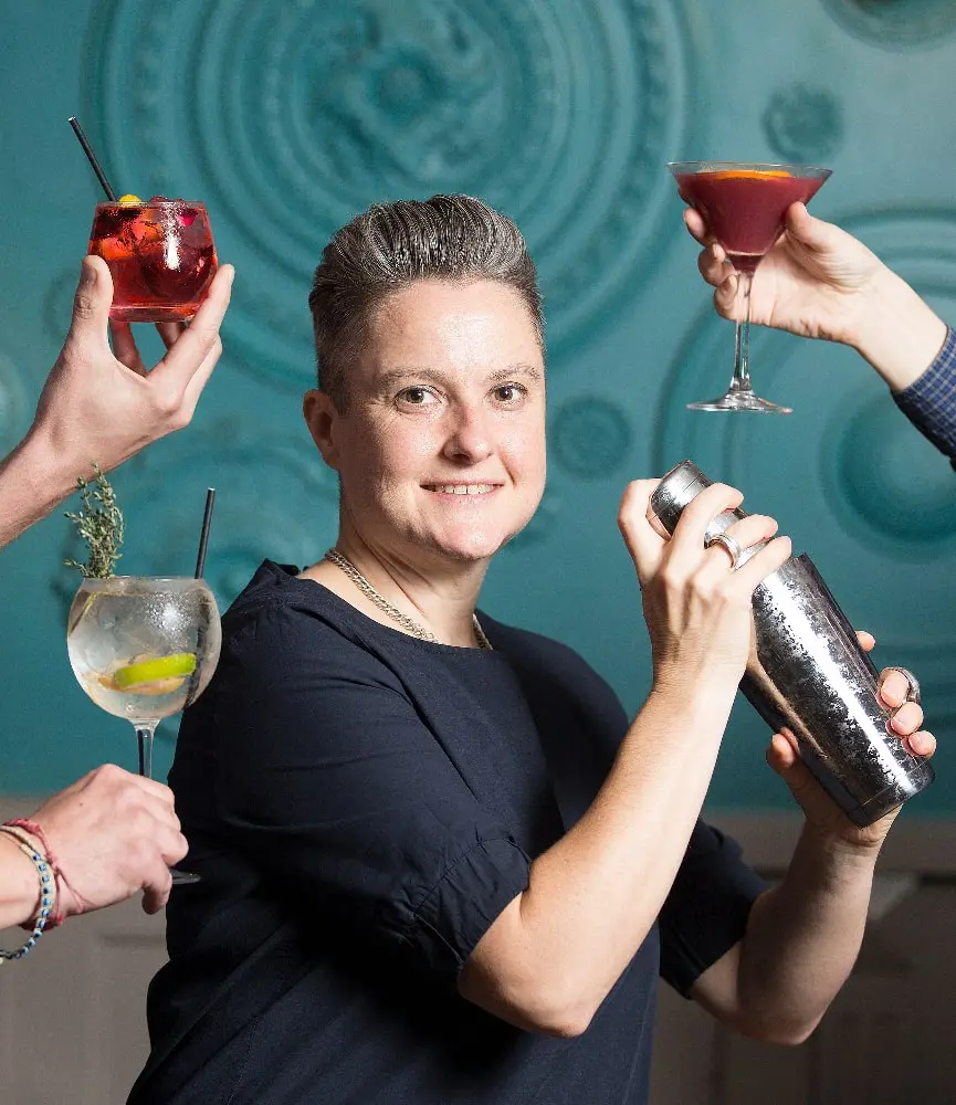 Laura is shaking a cocktail, with three hands around her holding cocktail glasses